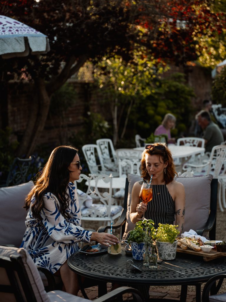 Two people sitting in Stanwell House garden bar eating and drinking new menu